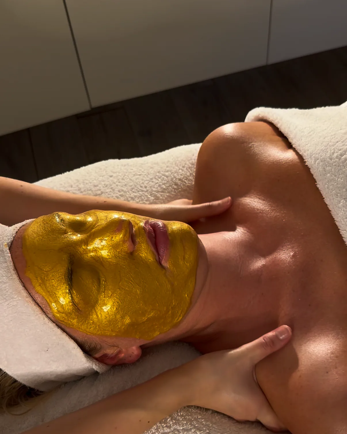 Eine goldfarbene Maske auf dem Gesicht, während die Schultern massiert werden
