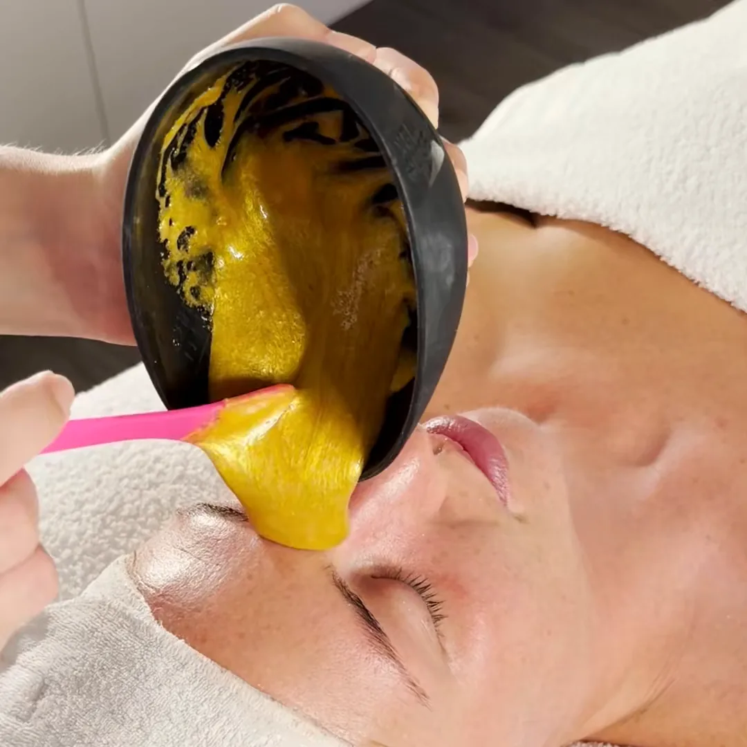 A gold-coloured mask runs from a small bowl onto a client's cheek