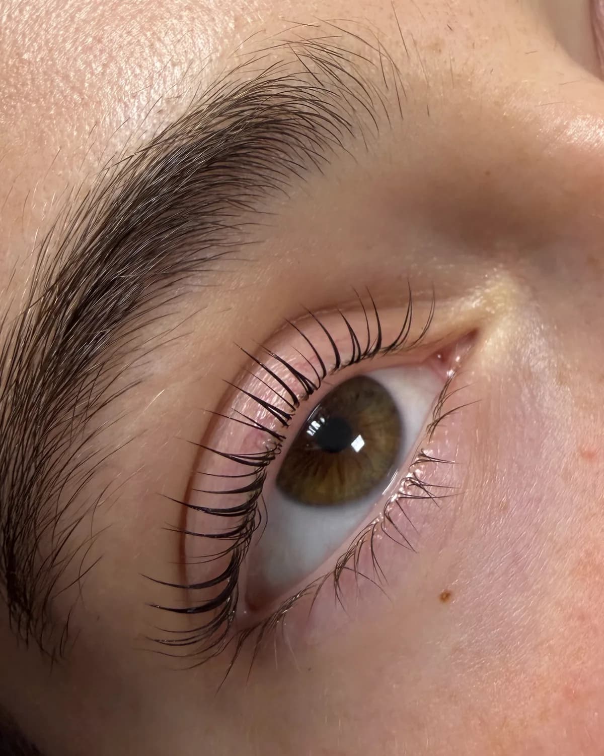 Een bruin oog met eigen wimpers die na een lash lift omhoog staan