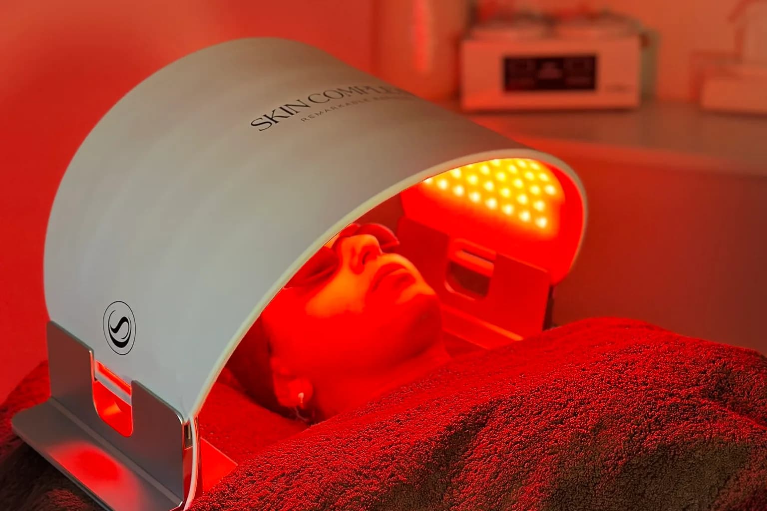 Een klant ligt met afgedekte ogen onder het LED-paneel van Skin Complete, dat rood licht geeft, in de behandelkamer van Moons Beauty