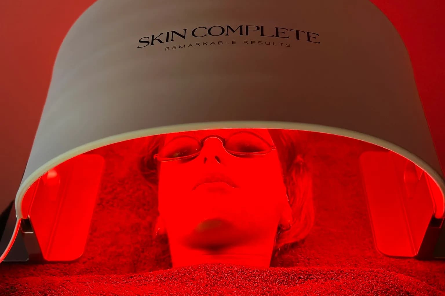 Een klant ligt met een beschermbril op onder het LED-paneel van Skin Complete, dat rood licht geeft