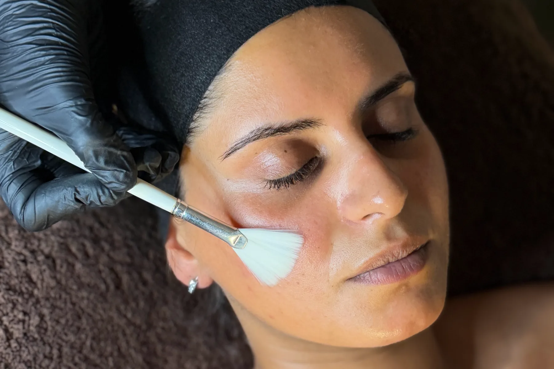 Met een waaierkwast wordt een peeling op de wang van een klant aangebracht