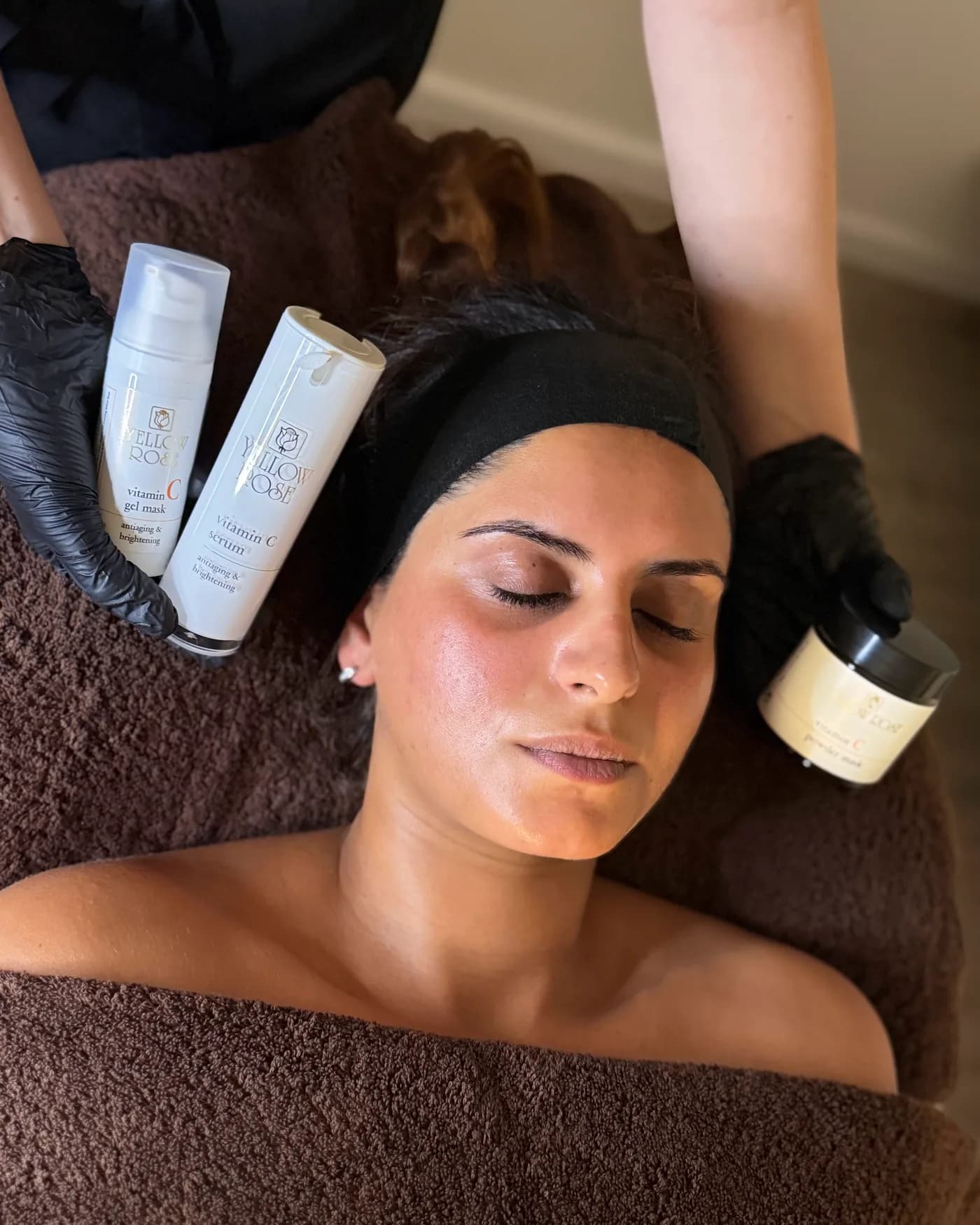 Het gelmasker, het serum en het poedermasker met vitamine C van Yellow Rose, naast het gezicht van een klant